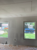 Interior renovation project by AMANES CONSTRUCTION in West Lafayette, Indiana, showing a living space with newly installed drywall, fully sanded, and ready for primer. Old flooring remains in place, highlighting the pre-painting stage before vinyl installation. Local residential remodeling and painting services.