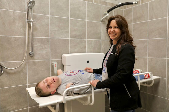 Mom standing next to an adult changing table. Son laying on adult changing table.