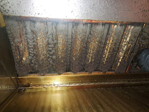 Grease-coated, burnt kitchen exhaust hood and filters, with a gloved hand at right, showing heavy grime and wear.