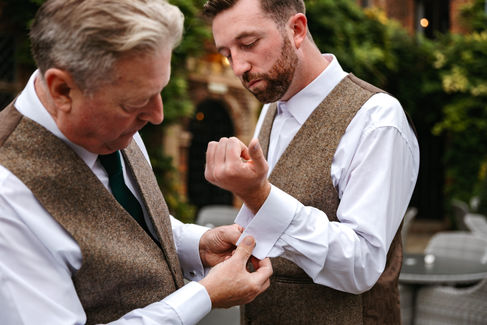 Father of groom helping groom with cuff links at Seckford Hall wedding 