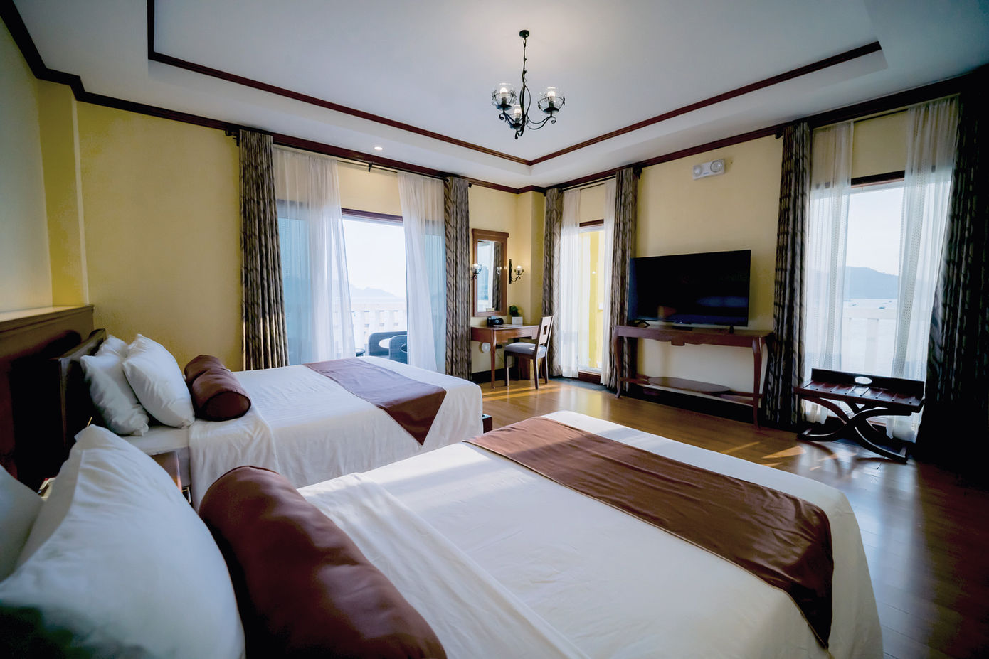 One king sized bed and one single bed against the wall with sunlight from the ocean view window hitting the floor and beds with Deluxe Room with Ocean View amenities around them