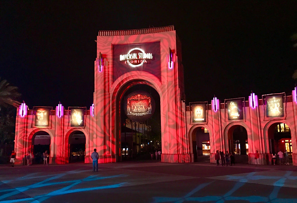 Entrance to Universal Studios Florida at night, lit in red with swirling patterns. Posters and "Halloween Horror Nights" sign visible.