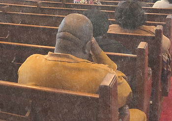 Man with hand to his head, sitting in a church pew, presumably in prayer.