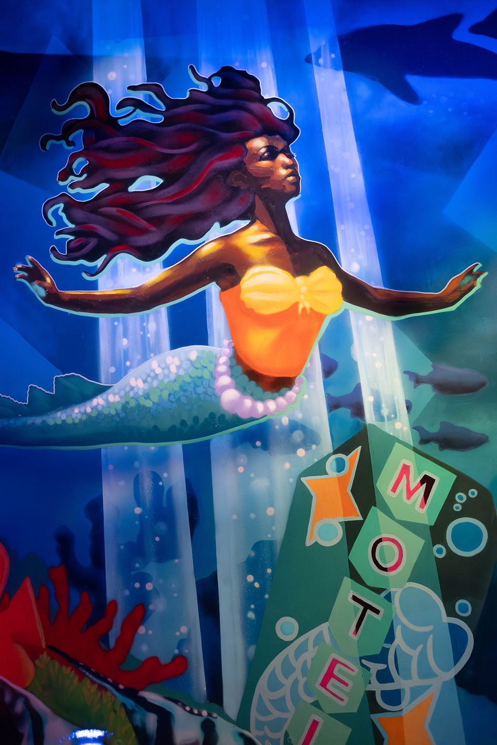 A radiant mural of a Black mermaid swimming near a motel sign, inspired by underwater Florida myths and legends.