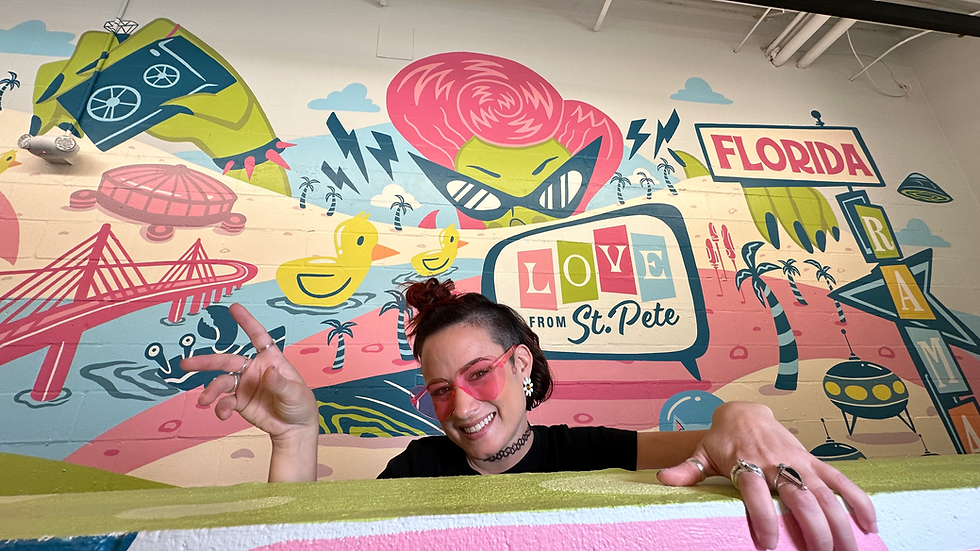 Ashley Cantero in pink glasses poses in front of a colorful mural with ducks, palm trees, and "Love from St. Pete" text. Bright, fun atmosphere.