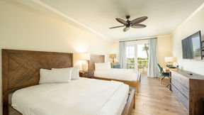 Two wooden beds with white linens in a bright room. Hotel room with a balcony with an ocean view at Grassy Flats Resort in Marathon, Florida.