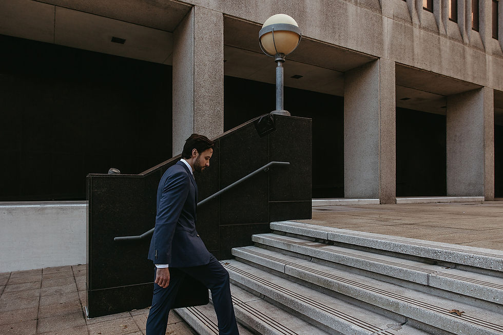 Man in blue suit ascending steps beside concrete building with columns. Mood is focused, setting urban.
