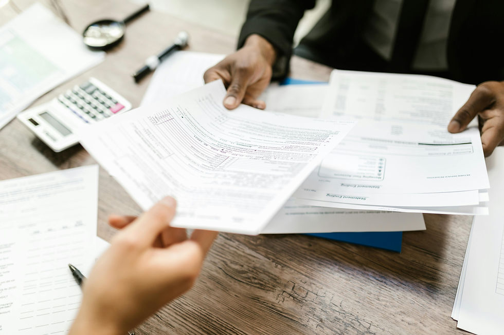 Hands exchange paperwork on a wooden desk with a calculator and pen nearby. The setting suggests a professional or office environment.
