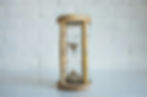 Wooden hourglass with sand, set against a white brick wall background, on a reflective surface.