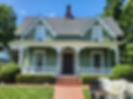 Sage green house with white gingerbread gables, wide porch, and a red brick walkway