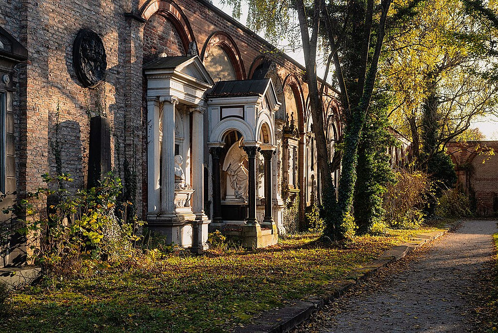 Alter Südfriedhof München im Herbstlicht; alte Gräber mit Säulen und Reliefs an einer Ziegelwand; ruhige, sonnige Atmosphäre mit Laub und Bäumen.