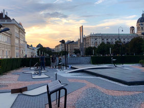 Minigolf Wien - Abendliche Minigolf Platz in Wien am Museumsquartier mit moderner Spiel- und Kunstinstallation, Menschen im Hintergrund, historische Gebäude und Sonnenuntergang.