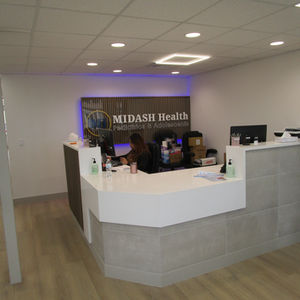 Completed MIDASH Health Front Desk modern style with white counter tops, wood flooring, gray slate and striped wood facade