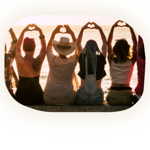 grupo de mujeres de espaldas frente ala playa levantando las manos haciendo un corazón.
