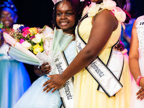 Asmara with her crown, sash, and flowers next to the other queen at the Miss Juneteenth pageant.
