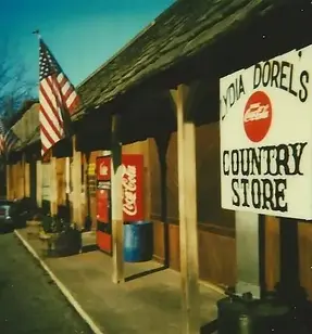 the location when it was a gas station in the 80s, viewed from the front corner of the building, with a sign that reads "Lydia Dorels Country Store" posted out front.