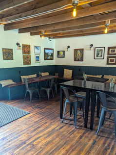 Tables and chairs in the corner of the bar with buyable art on the walls.