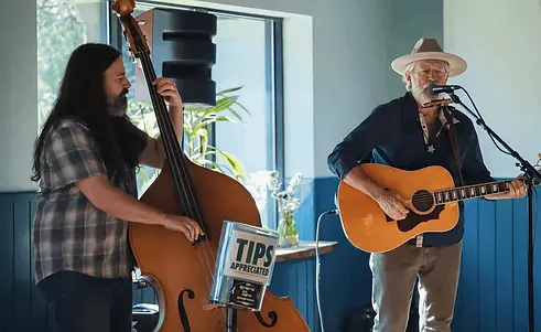 Man playing a cello and a man playing a guitar and singing in the corner of the bar.