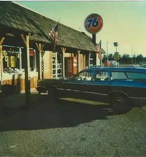 the location when it was a gas station in the 80s, viewed from the parking lot, with a station wagon parked out front.