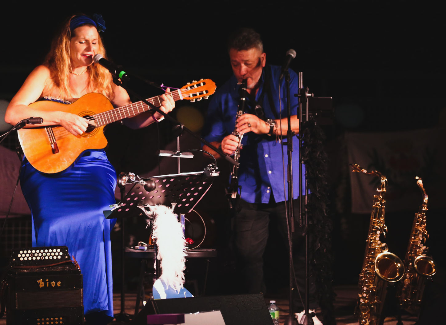Une femme chante et joue de la guitare, un homme joue de la clarinette sur scène.