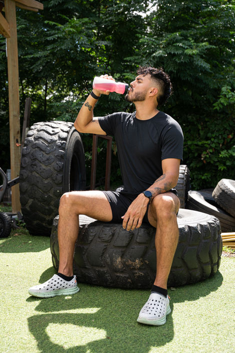 a man sits on a tire drinking from a pink bottle