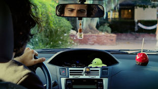 Two people in a car, looking surprised. The woman in the foreground, the man behind her. Black text "TRAVEL PLANS" at the top.
