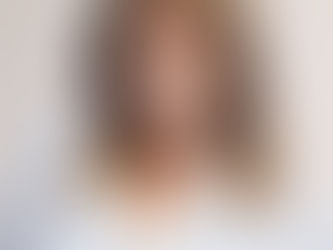 Smiling woman with wavy hair in a white shirt, wearing a star necklace. Light background, warm expression, conveys a joyful mood.