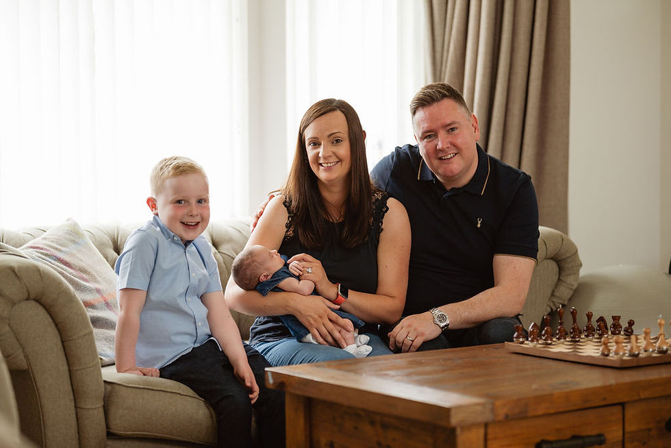 Mum, holding newborn baby, dad, young boy sitting on a couch in their home