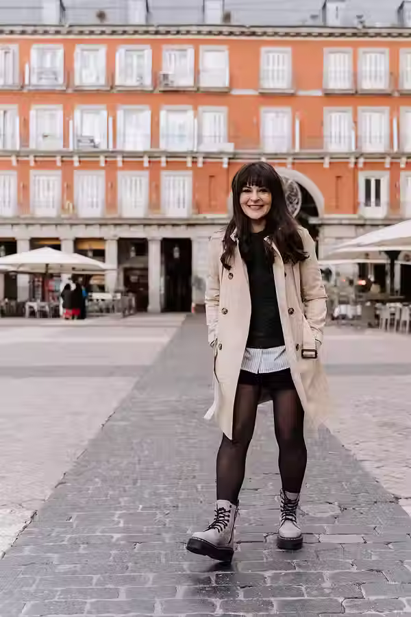 Woman posing in a winter outfit consisting of a trench coat and combat boots in the historic Plaza Mayor during a trip to Madrid.