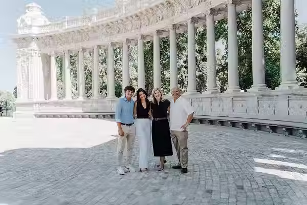 Family posing on the stone esplanade of the Monument to Alfonso XII, highlighting the imposing architecture of white columns in Retiro Park, Madrid.