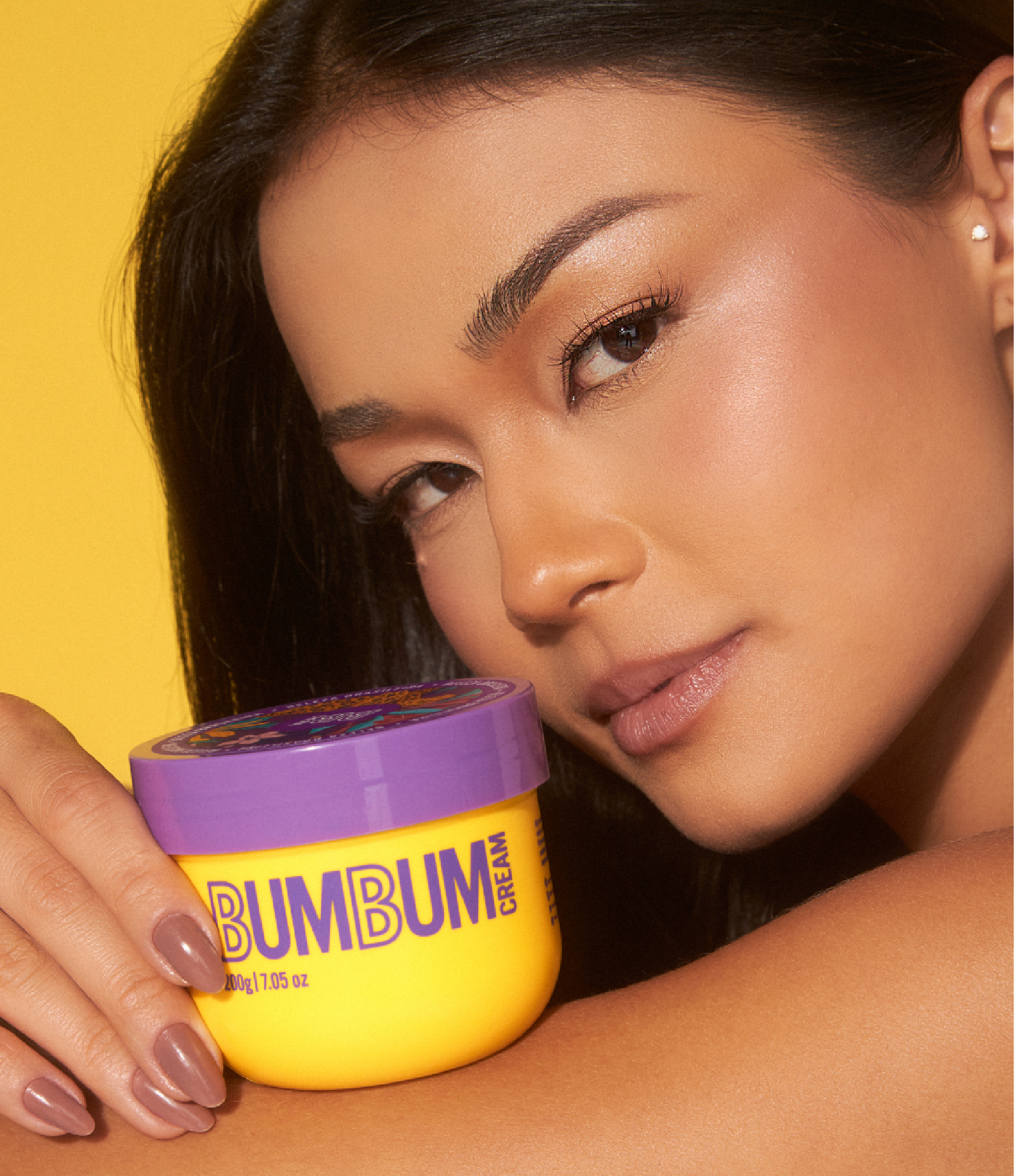 Jovem mulher segurando Bumbum Cream produto; Máscara corporal Beleza Brasileira bumbum cream 200G.