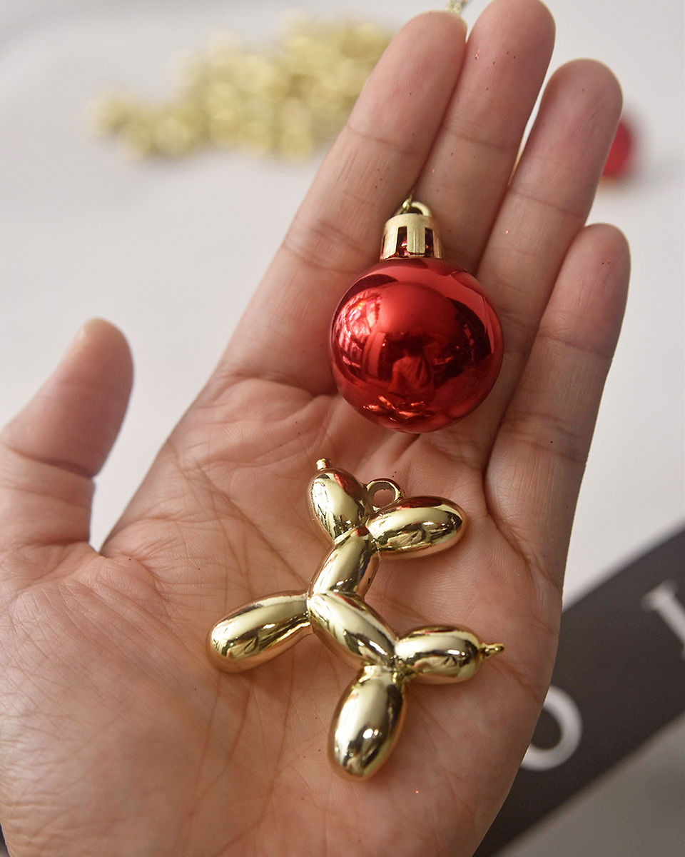 Hand holding a red Christmas ball and mini Jeff Koons-inspired balloon dog