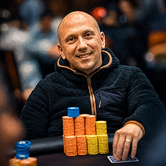 Nick Yunis smiling at a poker table with stacks of tournament chips during a live poker event.