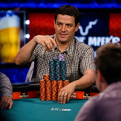 Carlos Mortensen seated at a poker table against a blue-lit background, wearing a black jacket and looking toward the camera.