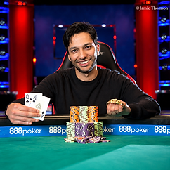 Mohsin Charania smiling at a poker table with playing cards, tournament chips and a WSOP bracelet.