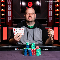 Maxx Coleman holding playing cards and a WSOP bracelet behind stacks of poker chips at the World Series of Poker.