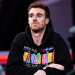 Adrian Attenborough seated at a poker table wearing a black graphic hoodie during a live tournament.
