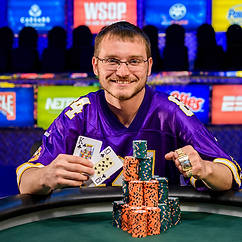 Kevin Eyster smiling at a poker table with tournament chips, playing cards and a championship ring after a major poker victory.