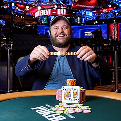 Scott Ball holding a WSOP bracelet at a poker table with chip stacks and pocket kings during a World Series of Poker event.