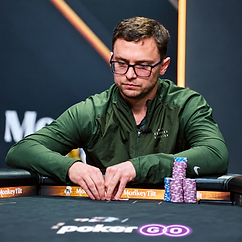 David Coleman competing at a high-stakes poker tournament, wearing glasses and a green jacket with stacks of tournament chips in front of him.