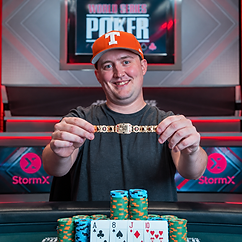 Michael Moncek holding a WSOP bracelet at a poker table with tournament chips and playing cards.