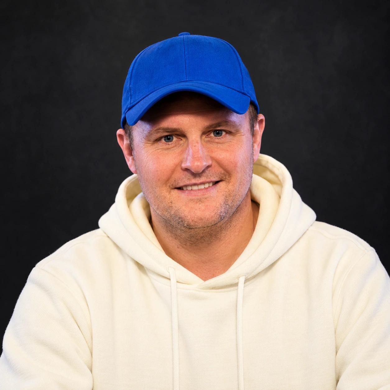 Editorial illustrated portrait of Tadhg Ryan wearing a blue cap and cream hoodie against a dark background.
