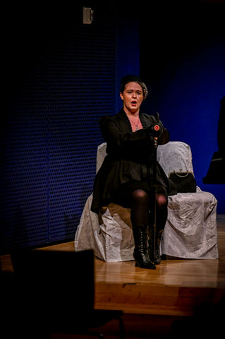 Singer in black dress seated, performing on stage
