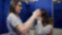 The GIF depicts an individual, likely an instructor, assisting a customer in putting on a virtual reality (VR) headset as part of Lowe’s Holoroom How To experience. The instructor is carefully adjusting the headset on the seated customer, who seems to be preparing for a virtual lesson on tiling a shower. This innovative VR clinic is designed to provide customers with a fully-immersive learning environment, enabling them to acquire home improvement skills such as tiling in a realistic yet controlled virtual setting. The background, with its simple blue partitions, suggests this demonstration is taking place in a dedicated space set up for this educational purpose.