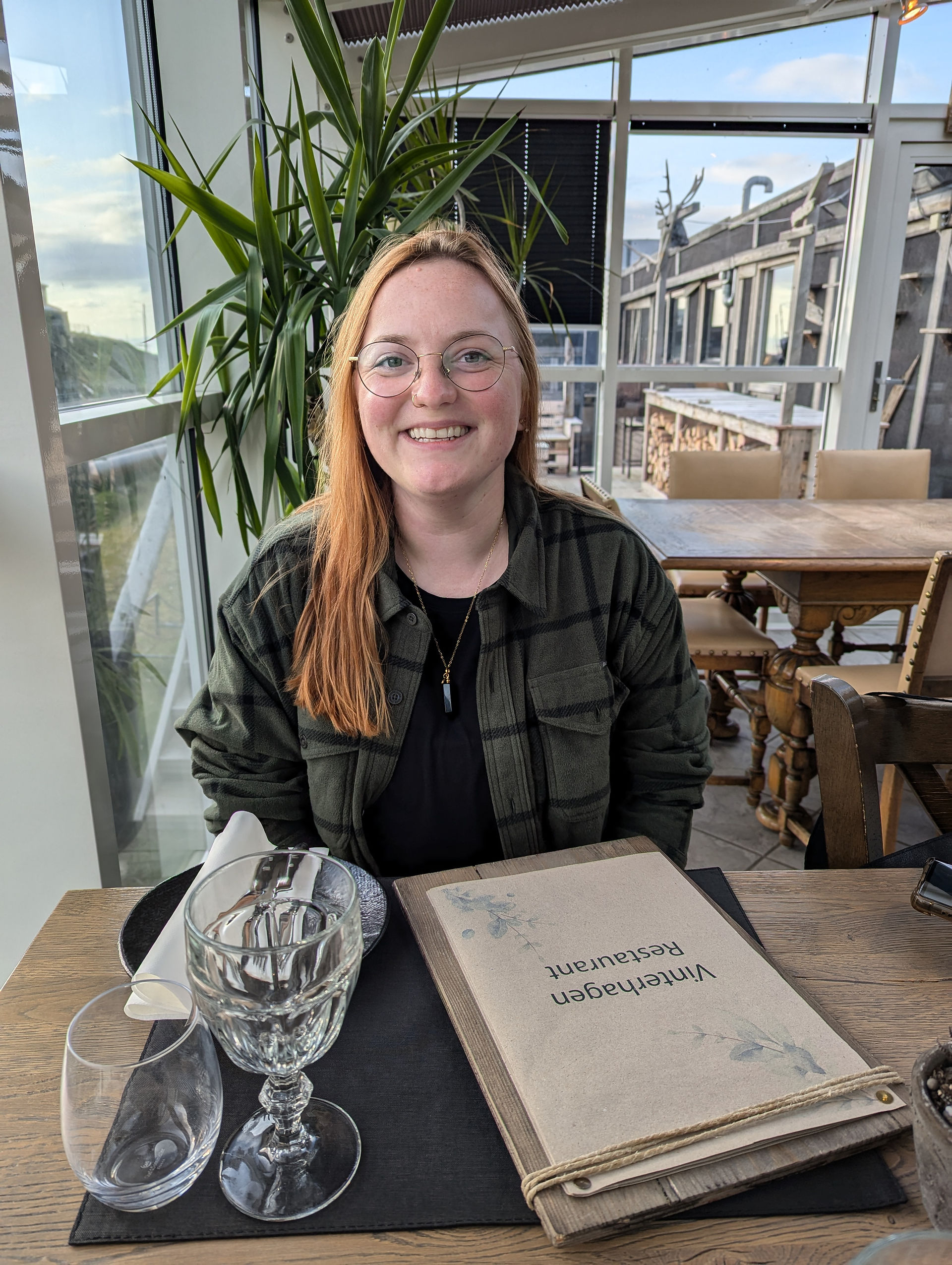 A woman with glasses sitting at a table with a menu in front of her that has text saying Vinterhagen Restaurant.