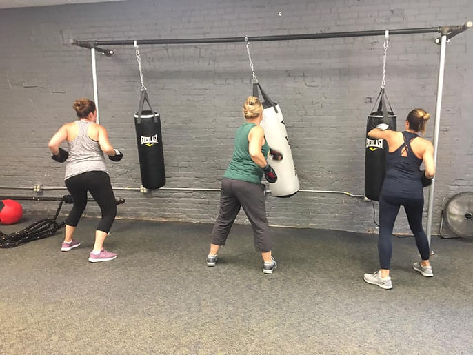 three women exercising with punching bags in bootcamp fitness class