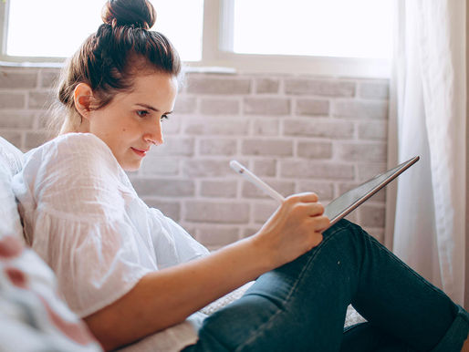 Woman entrepreneur wearing a white shirt and jeans on a couch working on tablet reviewing her DIY brand strategy at home