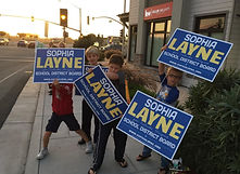Four kids holding up Sophia yard signs on a sidewalk