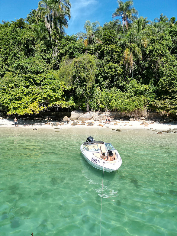 Barco em águas cristalinas com mata tropical ao fundo.