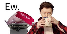 Corona sips coffee next to a blob fish at a typewriter. The fish wears a MAGA hat.